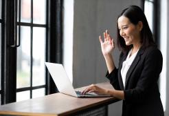 woman waving at colleagues on work laptop