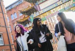 Three female students chatting and laughing while walking through Chinatown, Manchester