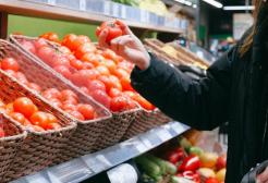 A person picking fresh red tomatoes from baskets in a supermarket produce aisle