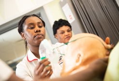 Female nursing student placing a nebulizer mask on a 'patient' manakin.