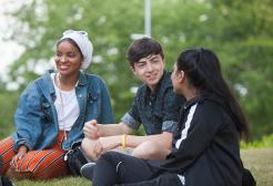 Three students chatting sat outside on grass