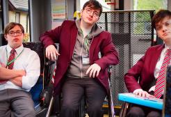 Three boys sit in a mobility bus in school uniform