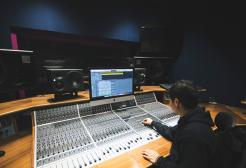Salford music degree student sitting by high-tech recording equipment in the university’s recording studio facilities.