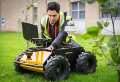 Student using wheeled surveying equipment and a laptop outdoors