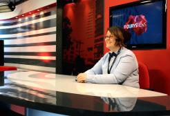 Student in Salford Quays new studio, sat at desk in front of news screen and smiling