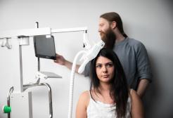  A researcher adjusts a computer monitor while a participant sits with a TMS (transcranial magnetic stimulation) device positioned near her head.
