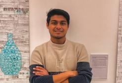 A male student wearing a jumper crossing his arms smiling at the camera