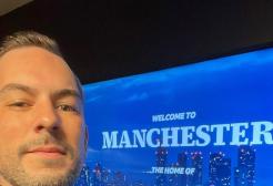 A man takes a selfie in front of a screen which reads welcome to Manchester the home of BBC Morning Live