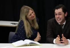 Two performers face an audience sat at a table on a stage 