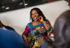 A female student in a bright dress touching her ear smiling looking to the side of the camera