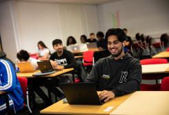 Students in classroom with laptops, one smiling male in focus