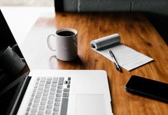 Desk with notepad, mobile phone, laptop and a cup of coffee
