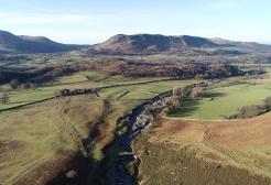Dried up riverbed cutting through fields, with hills in the background
