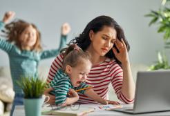 Mother trying to work on a laptop but distracted by two playing children