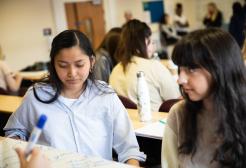 two female students in a classroom with other students in the background