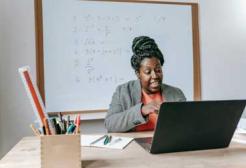 A learner sitting at a computer with maths problems on the whiteboard in the background
