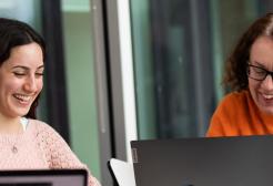 Two female students smiling whilst looking at their laptops