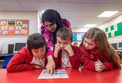 Female helper in headscarf helping pupils in school 