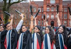 Graduates holding their scrolls outside the Peel Building, University of Salford