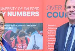 A student and an academic smiling in front of Salford banners 