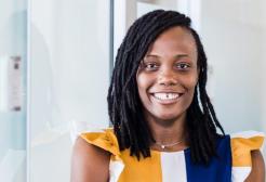 A headshot of Deborah wearing a yellow, blue and white dress