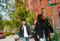 A group of four students walking through campus with Peel Park Quarter behind them