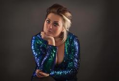 A woman in a blue sequin dress photographed against a black backdrop