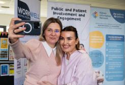 Two researchers smile as they take a selfie in front of roller banners