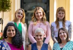 A line of six women pose in sets of three for a photo