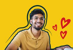A student holding a pen sits at a desk with an open book in front of him. His background is a yellow swatch with three cartoon hearts.