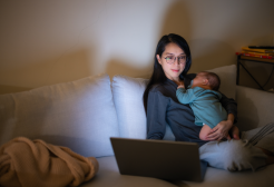 A mum sat working on her laptop while holding her child who is sleeping