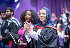A graduate stands during their ceremony and applauds while looking ta the stage smiling.