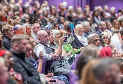 Guests in the audience of Graduation sit in purple seats and look at the stage. A couple in the middle look at the stage with emotional gazes.