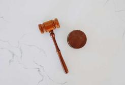 Wooden judge’s gavel resting beside a sound block on a light marble surface.
