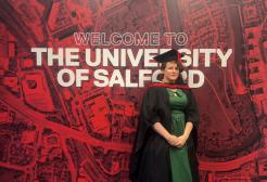 Nat Mulley is pictured in graduation cap and gown in front of a red background which says "The University of Salford"