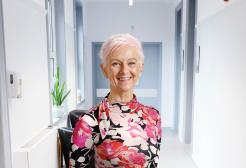 Fiona is pictured standing in a bright white corridor smiling at the camera
