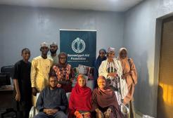 A group of people sat and stood surrounding a banner with their charity's logo on it