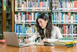 Student in a library studying with books and a laptop