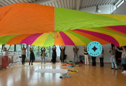 Group of people holding large multicoloured sheet above their heads.