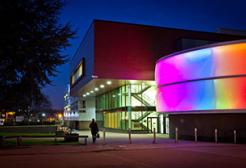 The Lady Hale building, a modern university building at night with a curved exterior wall illuminated by colorful lights, and a person walking nearby.