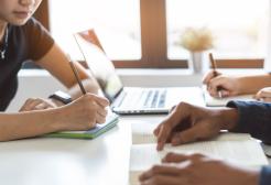 Students studying at a desk with a laptop and papers