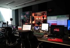 News studio gallery with multiple computer monitors and a large screen showing a presenter