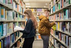 Two students selecting books from shelves in Clifford Whitworth Library