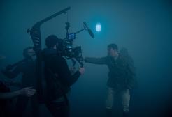 An actor holds a gun in a foggy sounds stage