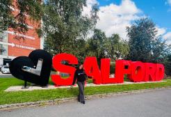 International Salford student in front of the Salford sign