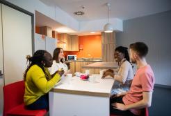 Group of four students sitting round a kitchen table eating and drinking