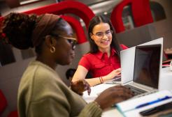 two students with their laptops sat smiling and talking
