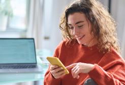 Woman using her smartphone besides a laptop on a table