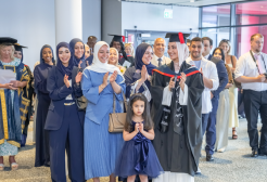 A crowd of people at a graduation ceremony, including graduates in black caps and gowns