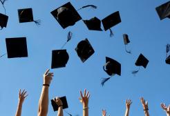 A wide shot of the arms of a group of people throwing graduation caps in the air